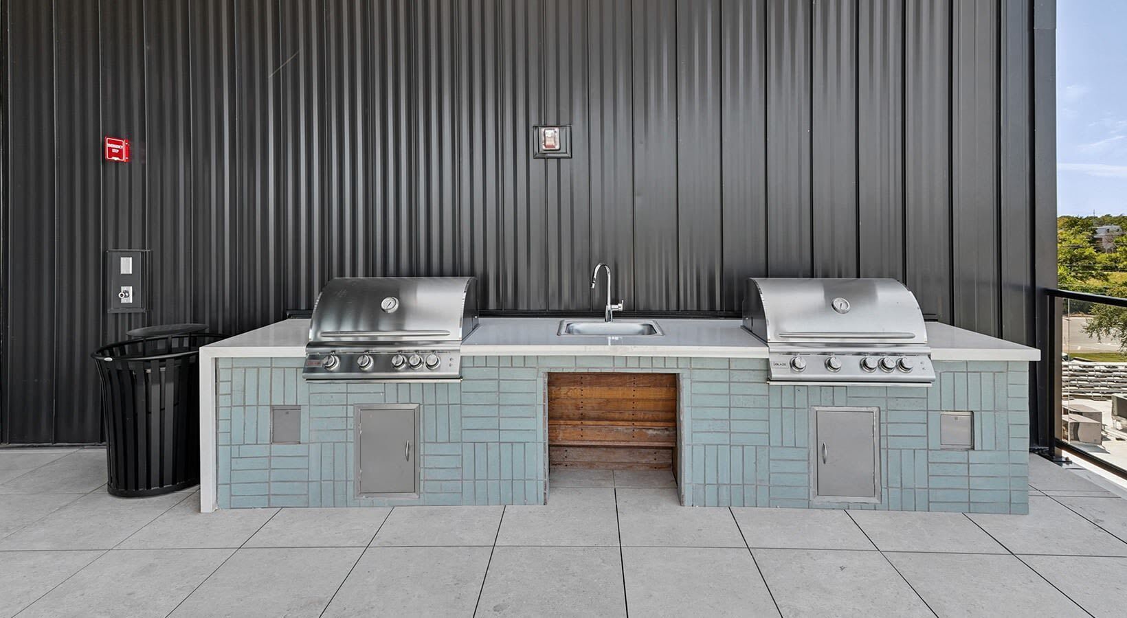 Une cuisine extérieure équipée de deux barbecues, d’un évier et d’une poubelle.