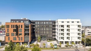 Un immeuble moderne à plusieurs étages, dont la façade est un mélange de briques et de verre, avec une entrée centrale surmontée d’un auvent en verre.
