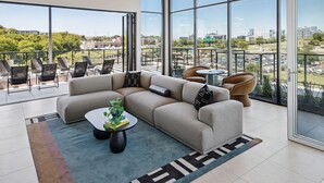 Un salon moderne avec un canapé d’angle, une table basse et une vue sur la ville grâce à de grandes fenêtres.