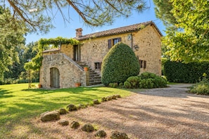 Una casa in pietra con una scala in pietra, un prato curato e un vialetto sterrato.