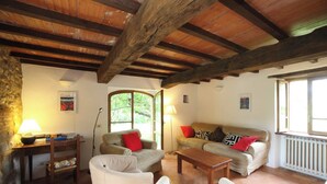 Ein gemütliches Wohnzimmer mit Steinwand, Holzbalkendecke, einer Sofagarnitur, einem Couchtisch und einer Lampe.