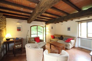 Ein gemütliches Wohnzimmer mit Steinwand, Holzbalkendecke, einer Sofagarnitur, einem Couchtisch und einer Lampe.