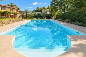 Ein rechteckiger Swimmingpool mit klarem, blauem Wasser, umgeben von einer Steinmauer und einer gepflasterten Terrasse.