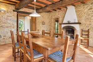 Una sala da pranzo rustica con un grande tavolo di legno, sedie, una lampada a sospensione e una parete in pietra.