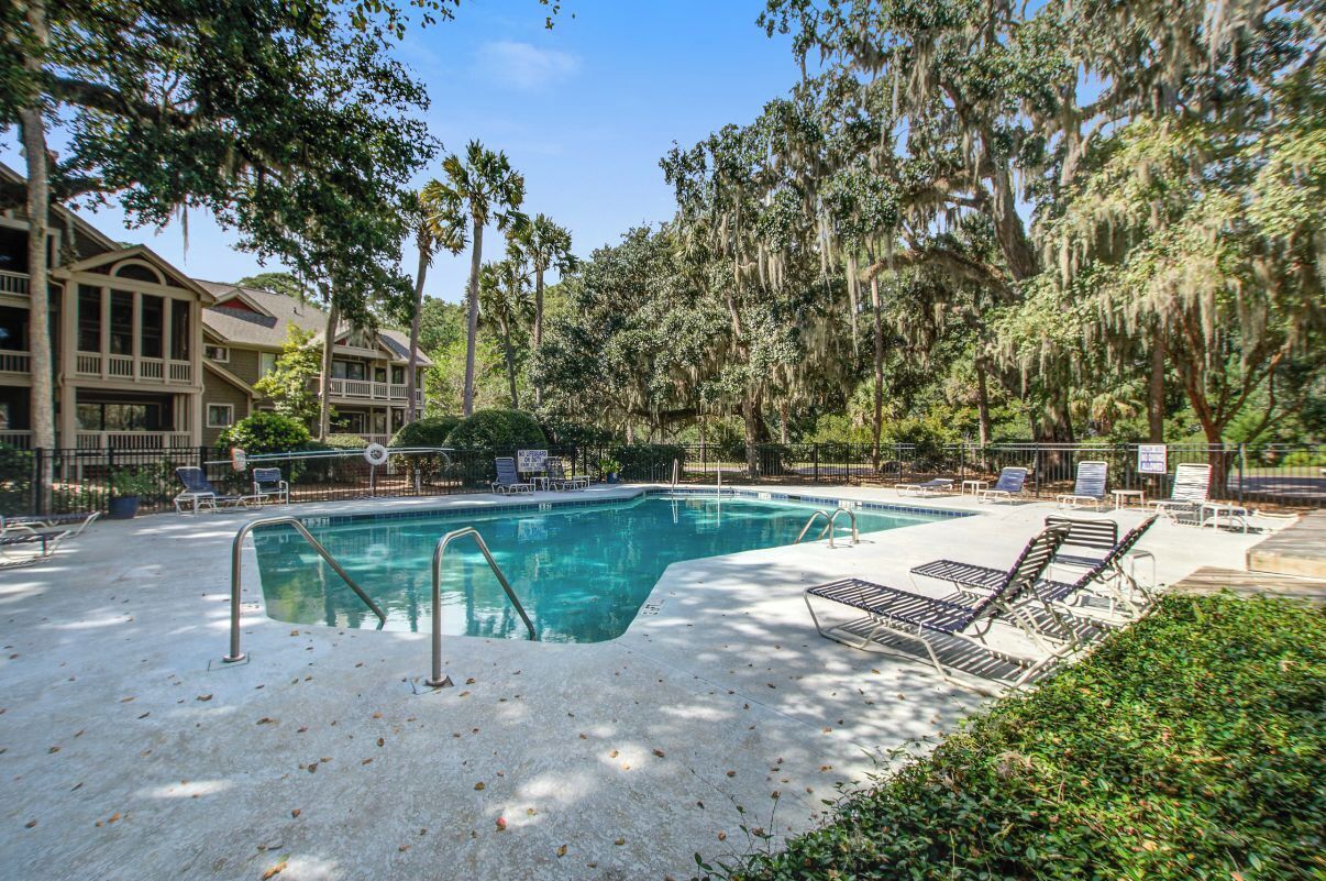 A swimming pool with lounge chairs, surrounded by trees and a building with balconies.