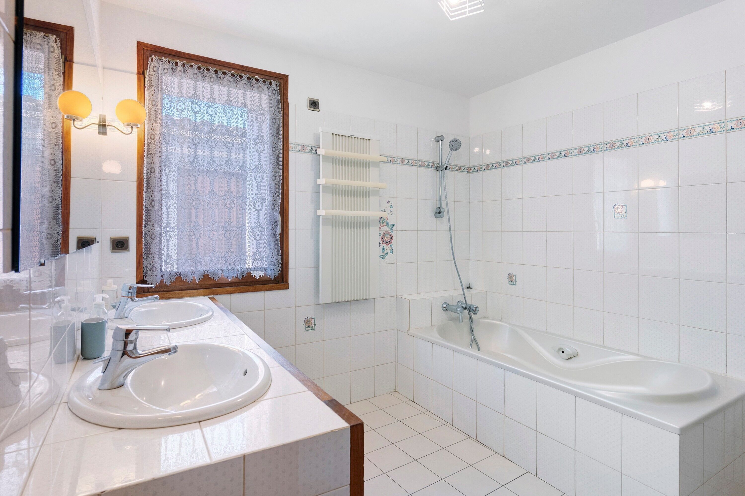 A bathroom with two sinks, a bathtub, a shower, and a window with lace curtains.