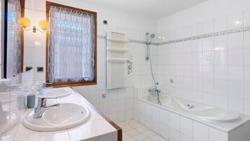 A bathroom with two sinks, a bathtub, a shower, and a window with lace curtains.