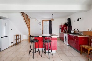 Cozinha com ilha central, dois bancos altos, máquina de lavar e escada.