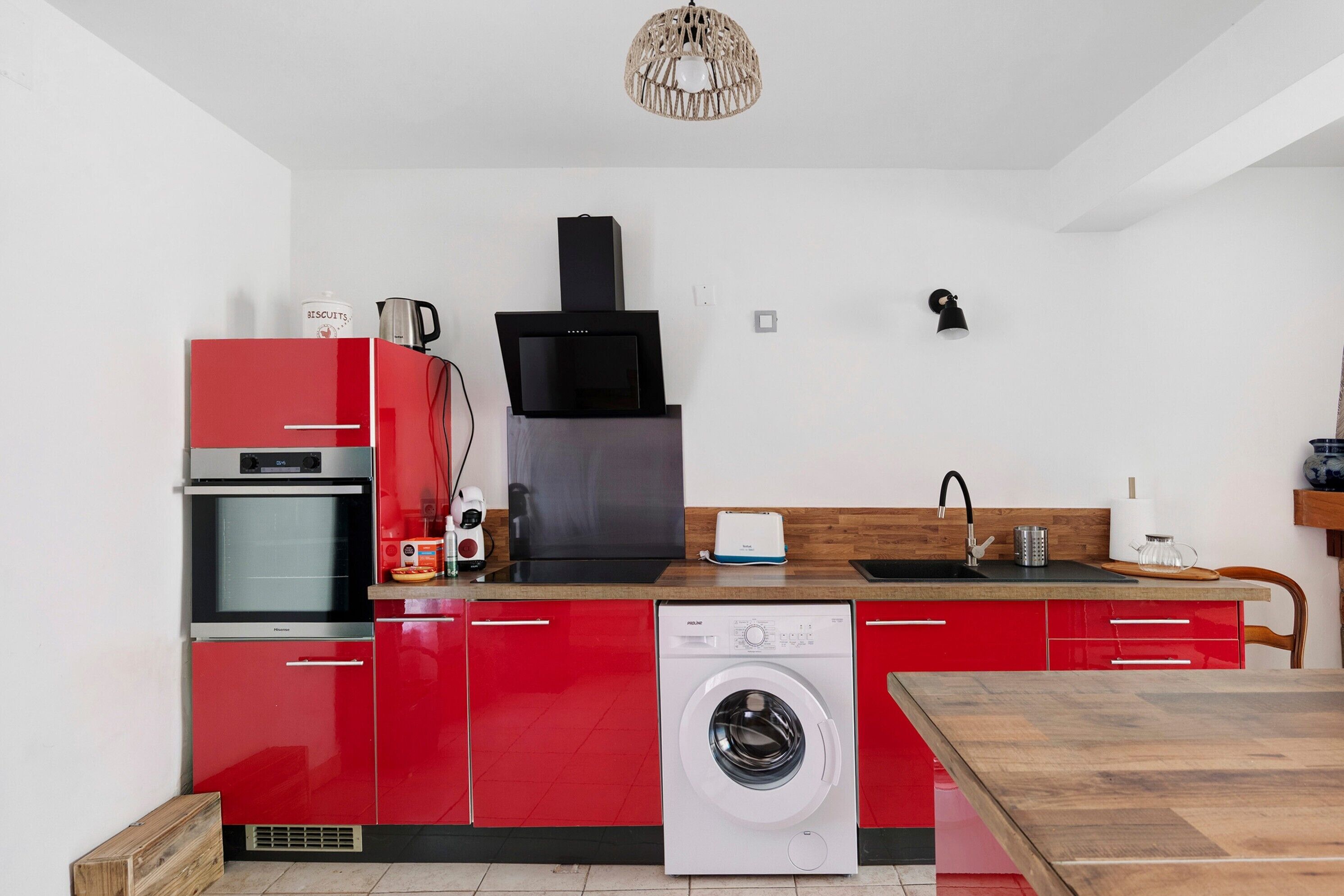 A compact kitchen with a red refrigerator, a built-in oven, a washing machine, and a black range hood.