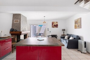 Cozinha com ilha vermelha, lareira de pedra e área de refeições com cadeiras.