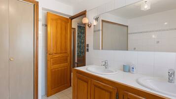A bathroom with two sinks, wooden cabinets, a large mirror, and a door leading to another room.