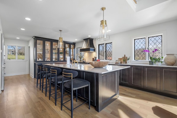 A modern kitchen with a central island, bar stools, pendant lighting, and a view of the outdoors.