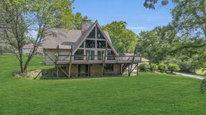 A two-story house with a stone foundation, a wooden deck, and a large front window.