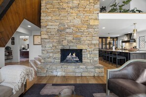 A stone fireplace with a fire, a wooden ceiling, a bar area, and a seating area with a sofa and a chair.