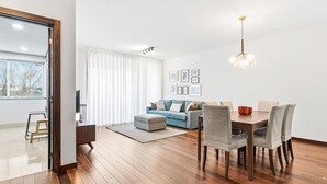 Ein modernes Wohnzimmer mit Holzboden, einer Couch, einem Esstisch mit Stühlen und einer Deckenleuchte.