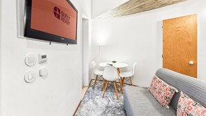 A modern room with a flat-screen TV, a wooden door, a round table with chairs, and a grey sofa with patterned cushions. - GuestReady - The Traveler’s Island (Porto)