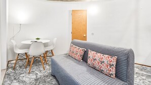A compact living space with a gray sofa, two white chairs, a small round table, and a wooden door. - GuestReady - The Traveler’s Island (Porto)