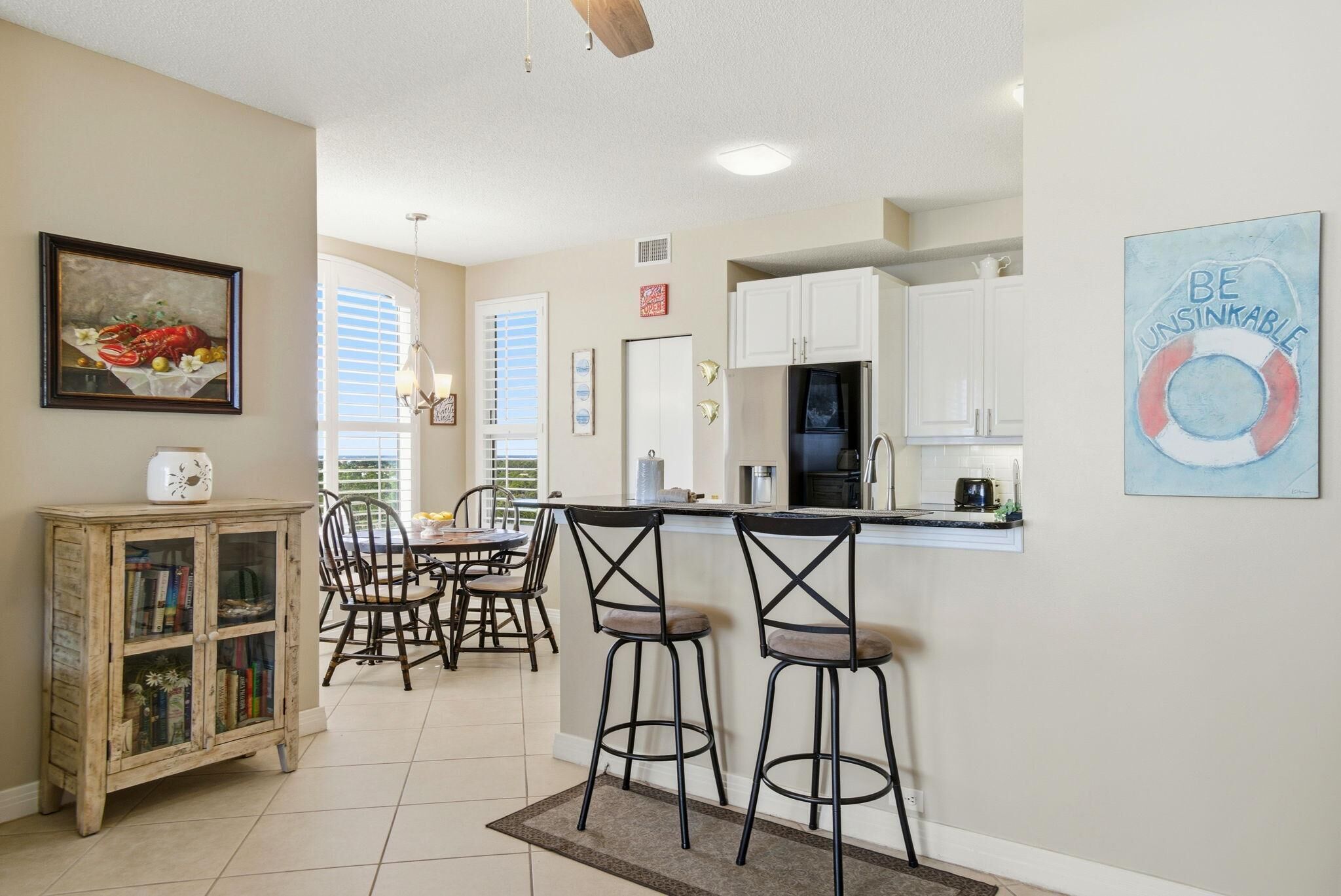A kitchen with a dining area, white cabinets, a bar stool, and a painting on the wall.