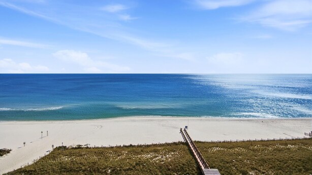 A beach with a wooden boardwalk leading to the shore, clear skies, and calm ocean waters. - Beach Colony East 8D (Pensacola)