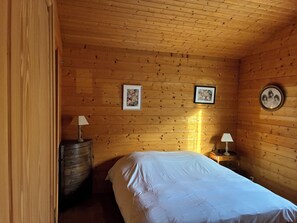 A wooden-paneled room with a bed, two framed pictures on the wall, and a small table with a lamp. - 140m2 family chalet, 100m from the lake and quiet center, renovated in 2026. (Gérardmer)
