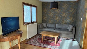 Ett vardagsrum med en tv, en soffa, ett soffbord och tapeter med ett mönster.