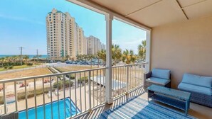 A balcony with a view of a swimming pool, a beach, and tall buildings. - Grand Caribbean West 310 (Pensacola)