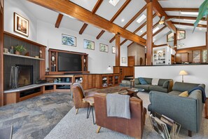 Ein geräumiger Wohnbereich mit Kamin, Holzbalken, einem großen Fernseher und bequemen Sitzmöglichkeiten.