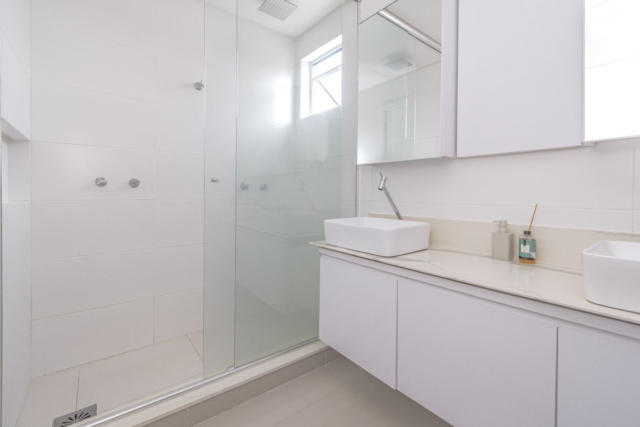 A modern bathroom with a glass shower enclosure, white tiles, and a countertop with a sink and toiletries.