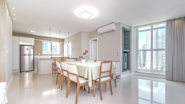 A modern kitchen with a dining area, large windows, and a view of the city. - Apartamento no Centro com 3 su tes a 400m da Praia (Balneário Camboriú)