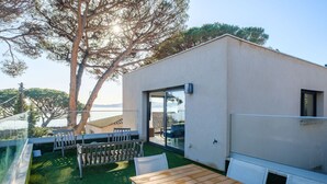 En moderne udendørs terrasse med et træbord og stole, et glasgelænder og havudsigt.