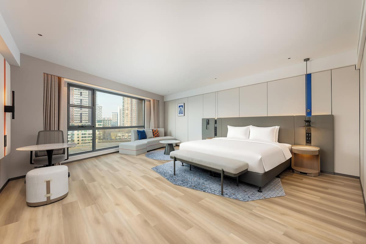 Een moderne hotelkamer met een groot bed, een bureau, een bank en uitzicht op de stad.