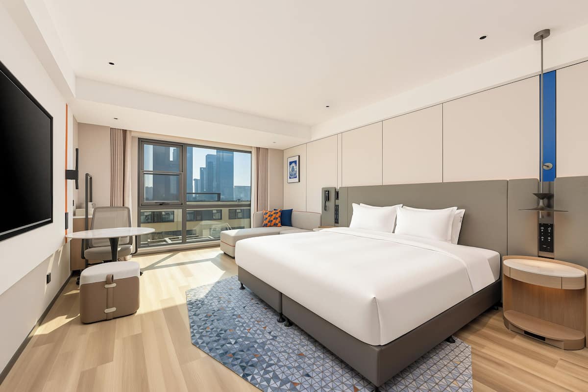 Een moderne hotelkamer met een groot bed, een bureau, een stoel, een televisie en uitzicht op de stad.