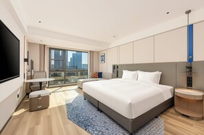 Ein modernes Hotelzimmer mit einem großen Bett, einem Schreibtisch, einem Stuhl, einem Fernseher und Blick auf die Stadt.