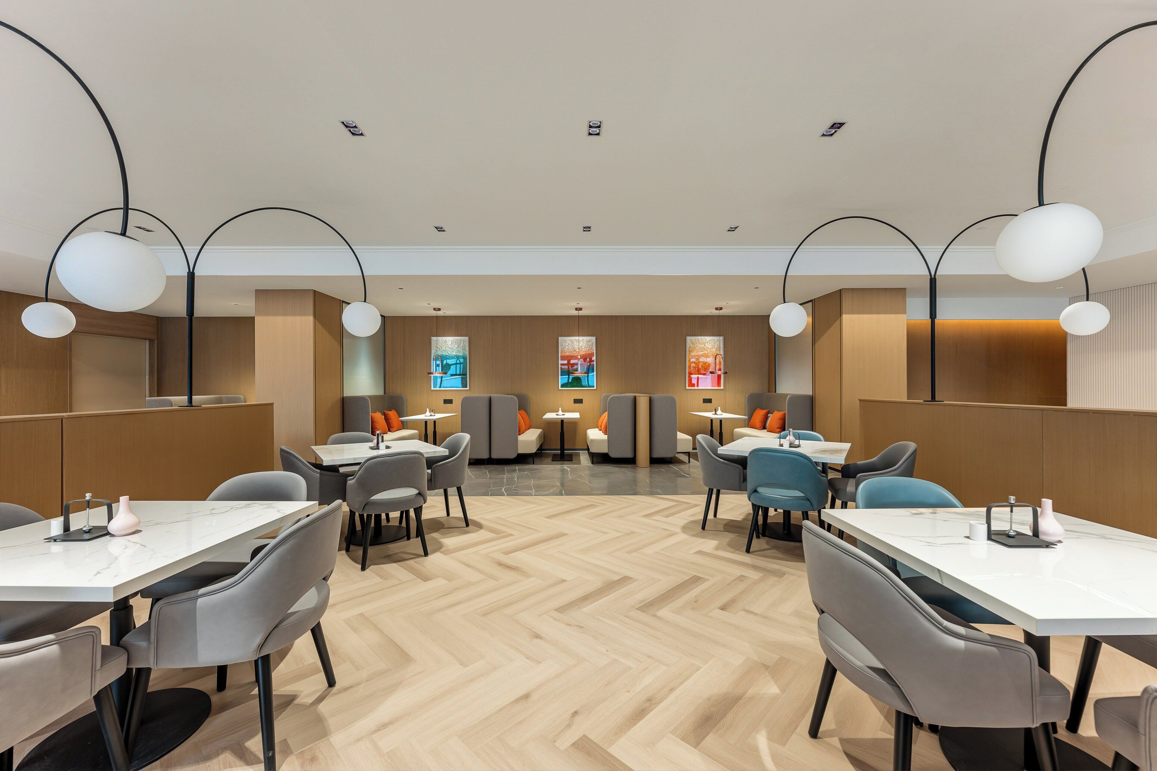 Un comedor moderno con varias mesas y sillas, paneles de madera en las paredes e iluminación colgante.