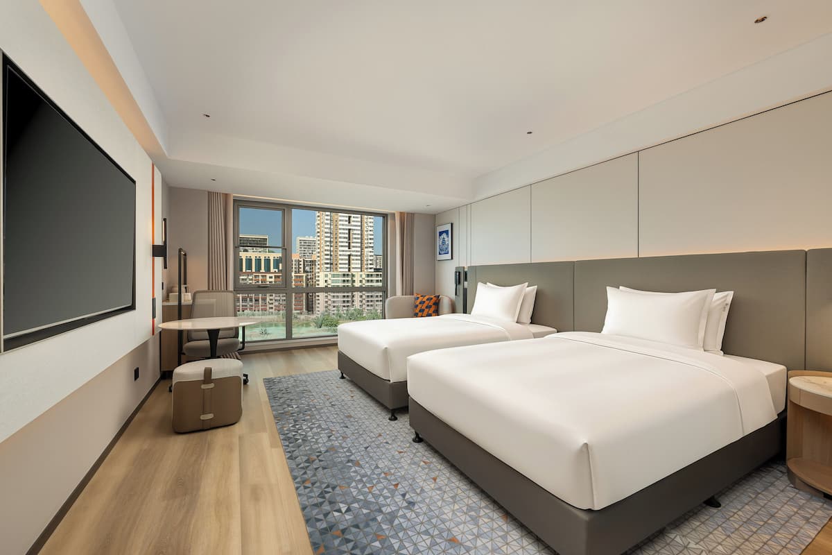 Een moderne hotelkamer met twee bedden, een groot raam, een bureau en uitzicht op de stad.