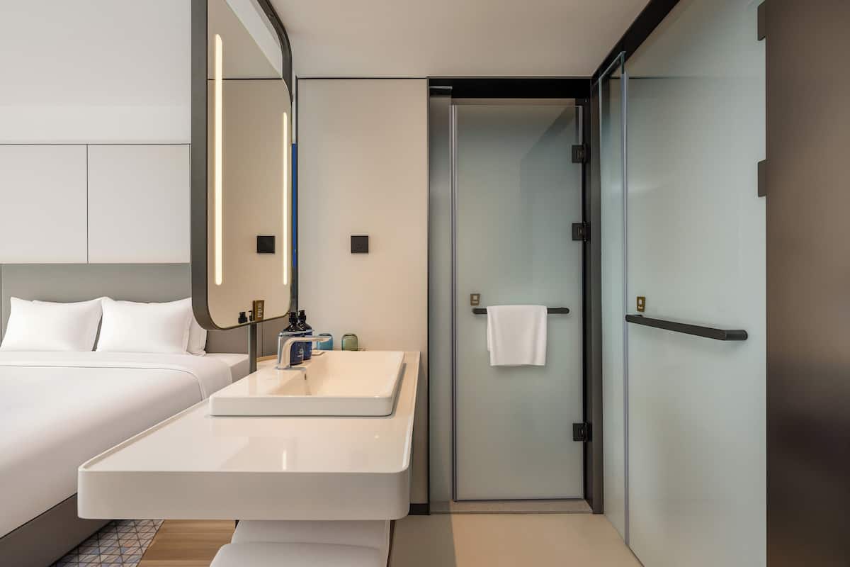 Een moderne hotelkamer met een groot bed, een badkamer met een wastafel en een glazen deur naar een douchecel.