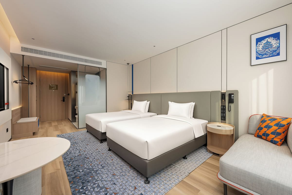 Een moderne hotelkamer met twee bedden, een bank, een eettafeltje en een telefoon aan de muur.