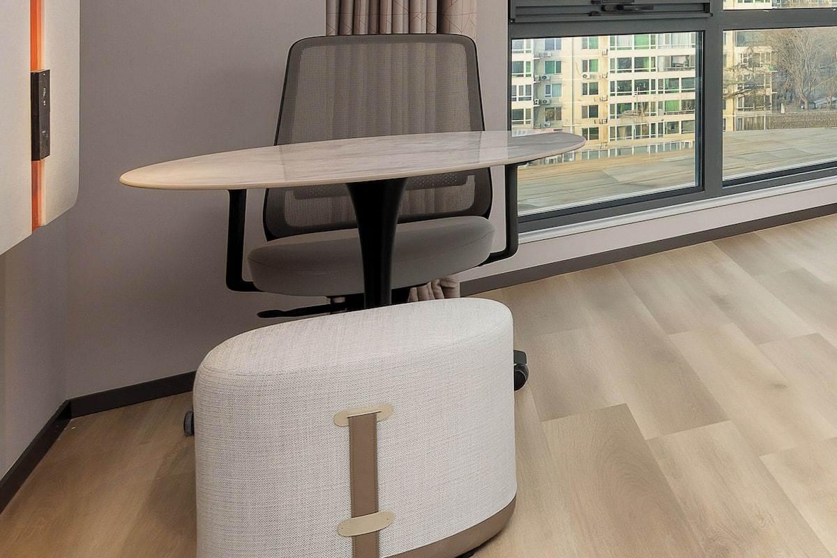 Een moderne kantoorruimte met een ronde tafel, een bureaustoel en een groot raam met uitzicht op gebouwen.