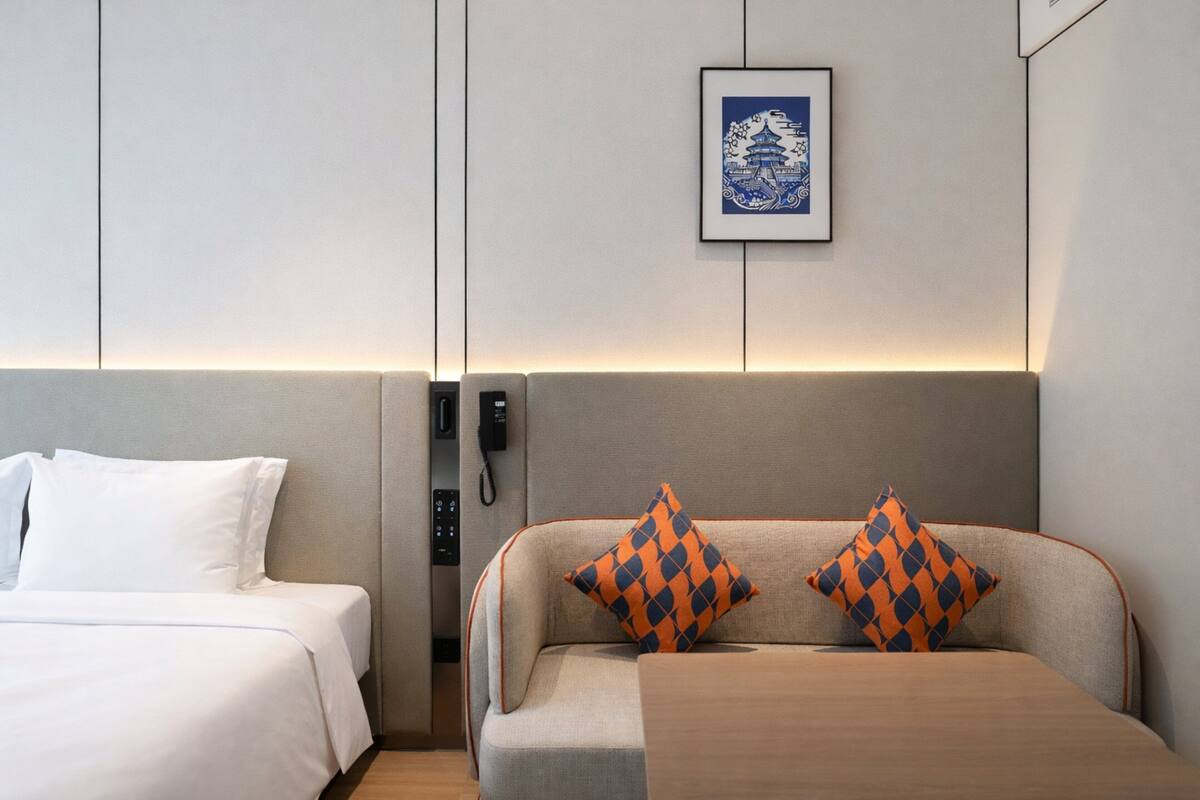 Een hotelkamer met een bed, een bank, een ingelijst kunstwerk aan de muur en een telefoon.