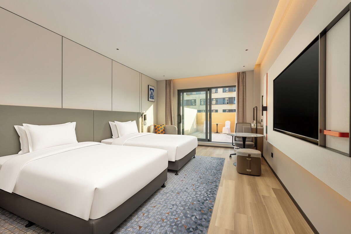 Een hotelkamer met twee bedden, een televisie, een tafeltje en uitzicht op buiten.