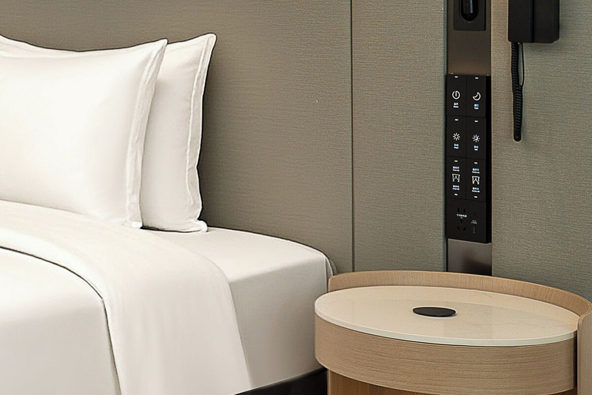 Una habitación de hotel moderna con cama, mesita de noche y teléfono instalado en la pared.