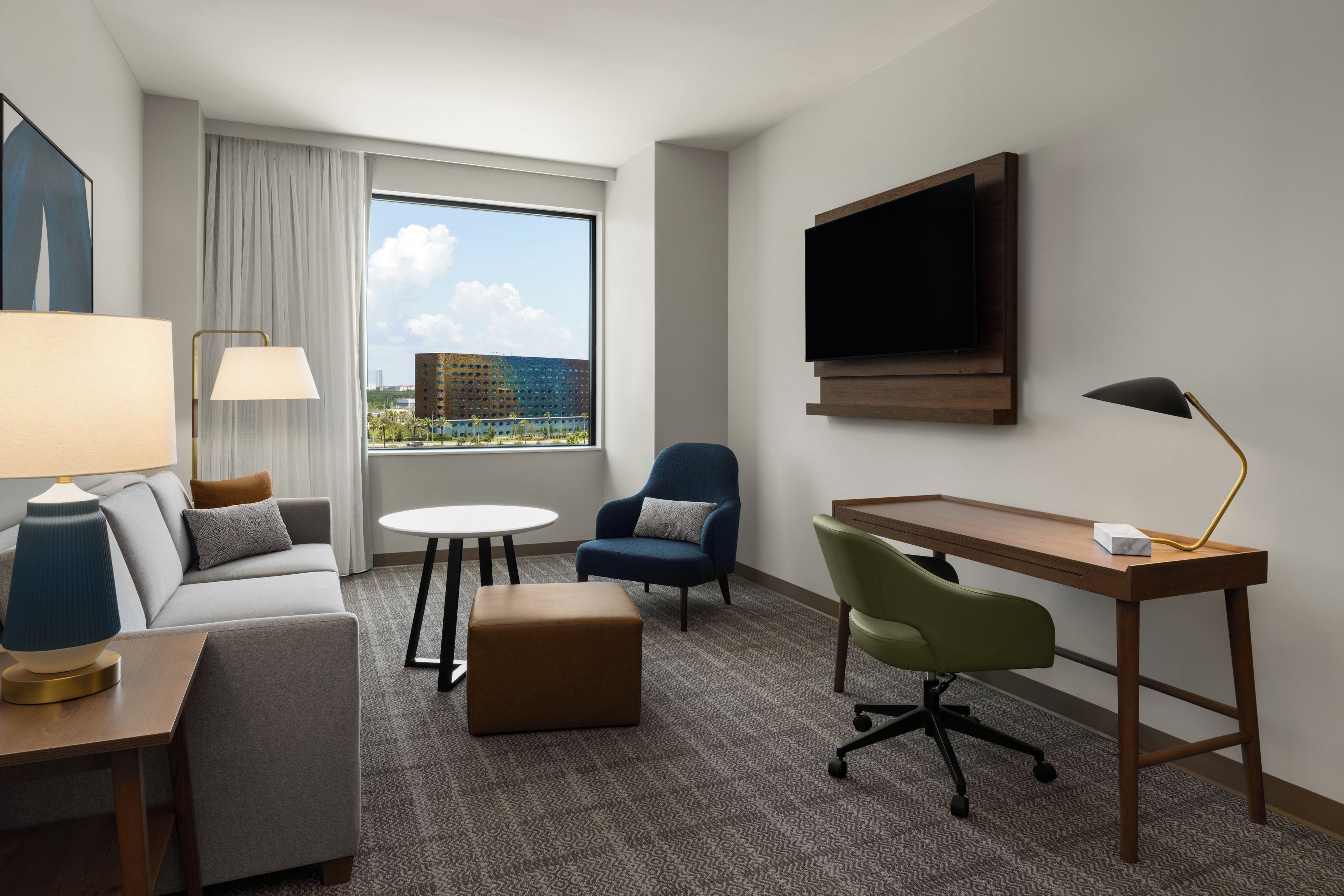 Une chambre d’hôtel équipée d’un canapé, d’un fauteuil, d’un bureau et d’un téléviseur fixé au mur.