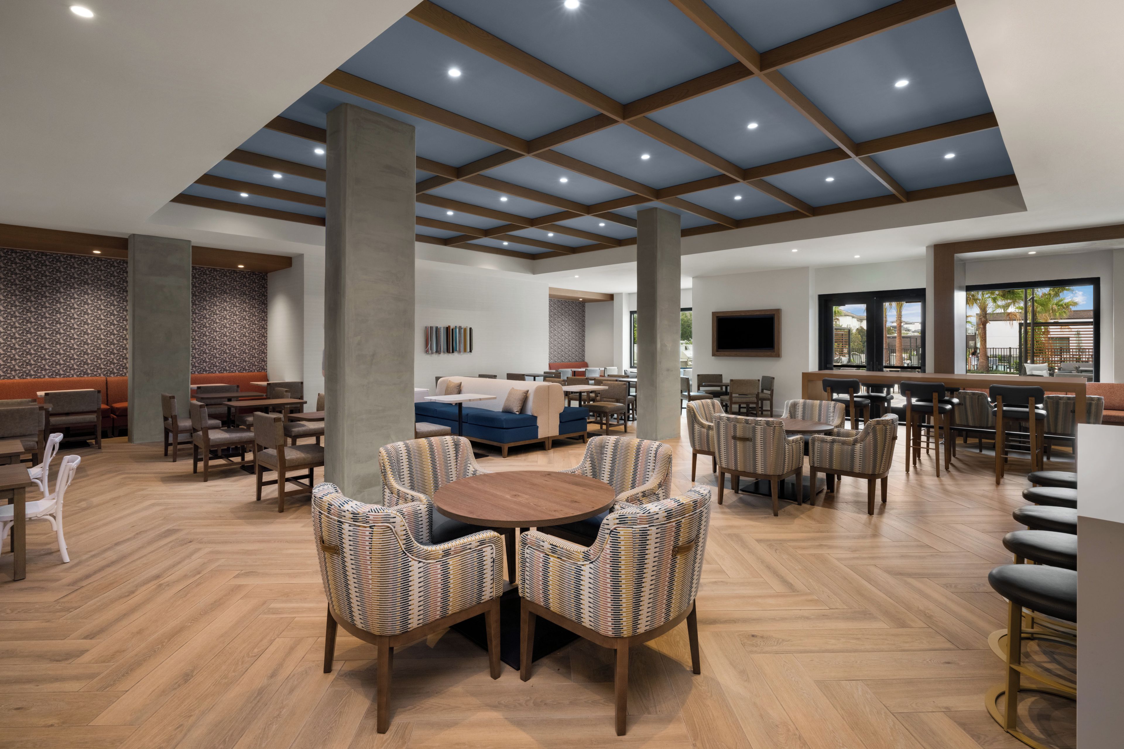 A spacious indoor area with a high ceiling, wooden beams, and a mix of seating arrangements including tables, chairs, and sofas.