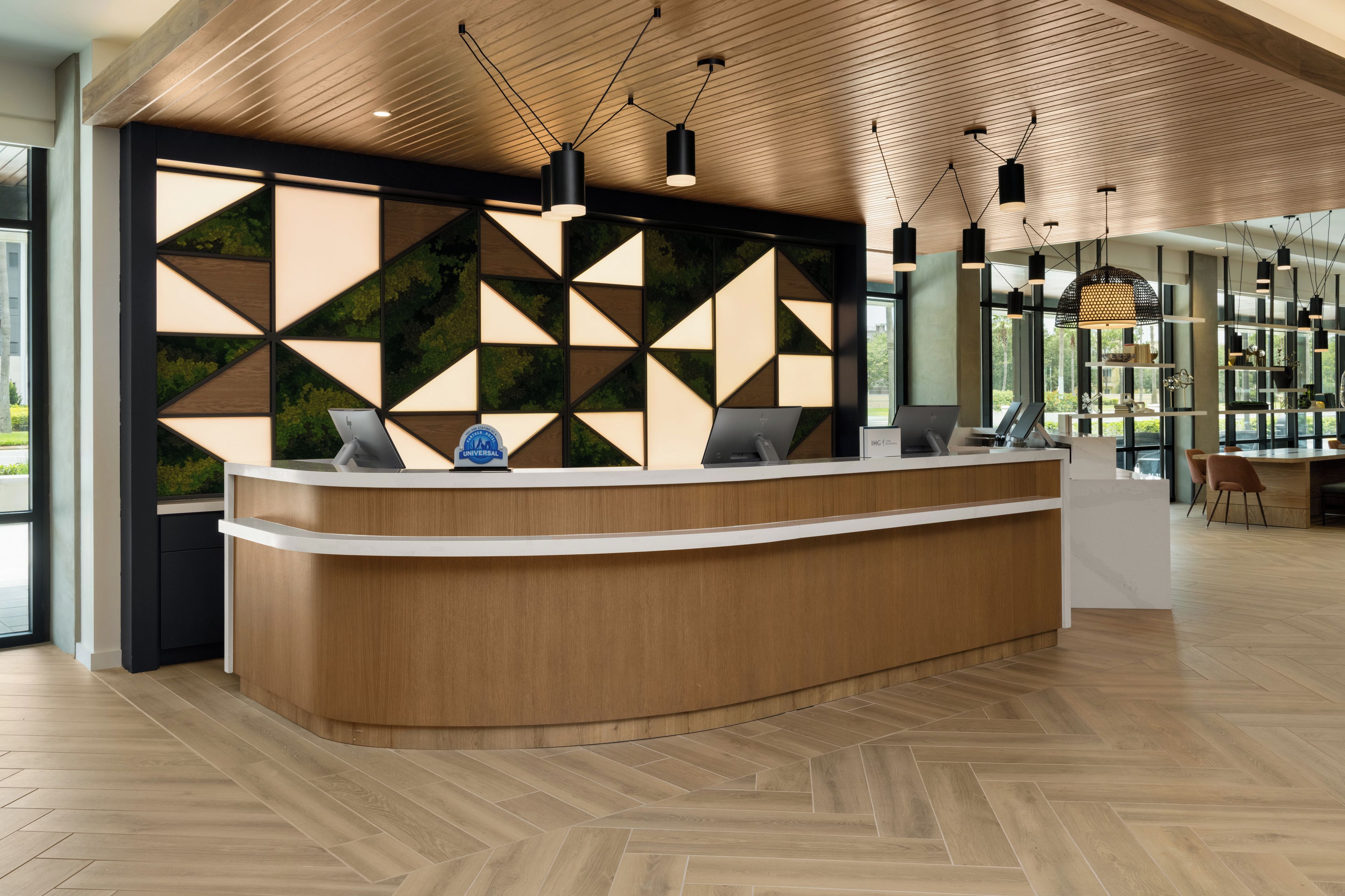 A reception desk with a geometric wall design, a wooden ceiling, and pendant lighting.