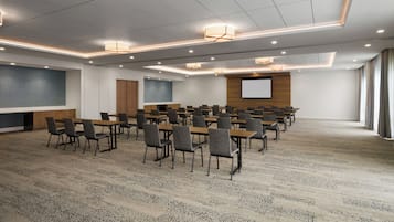 A conference room with a large screen, multiple tables, and chairs arranged for meetings.