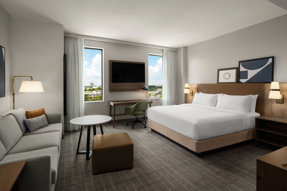 Una habitación de hotel con cama, escritorio, silla, sofá y televisor.