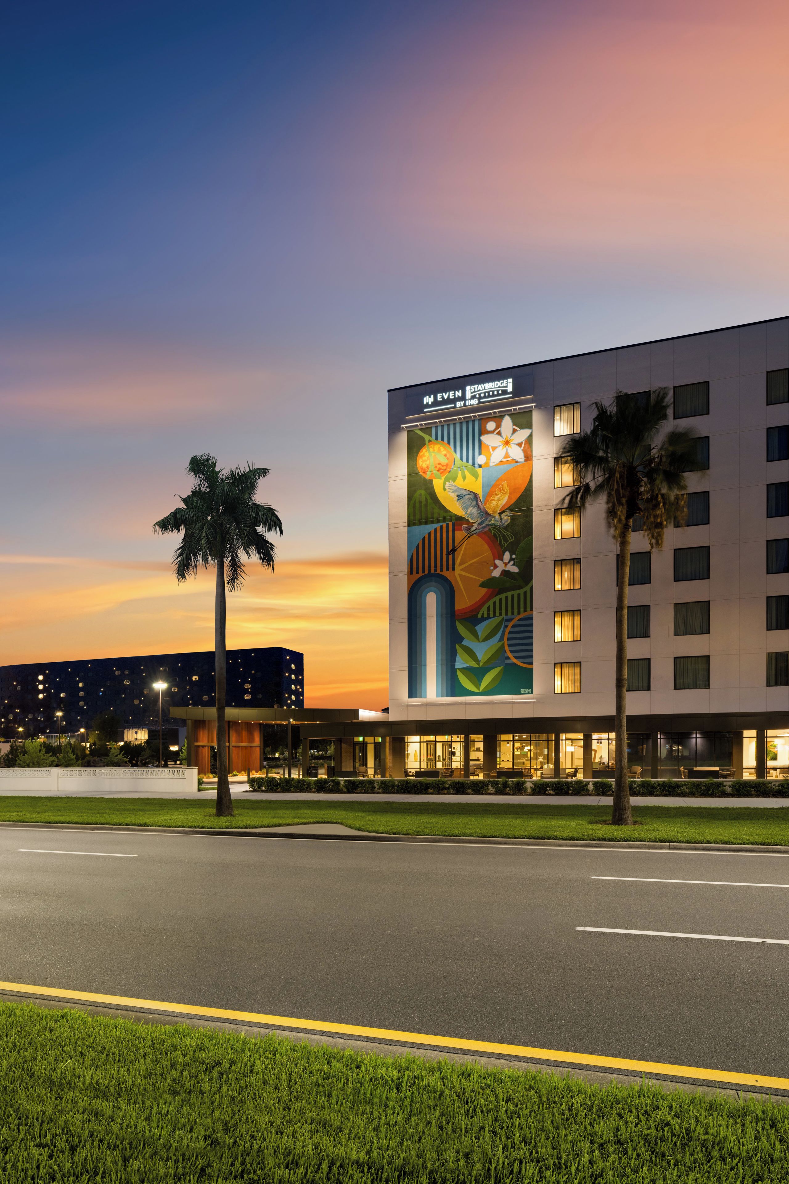 A hotel with a large mural on the side, a parking lot, and palm trees.
