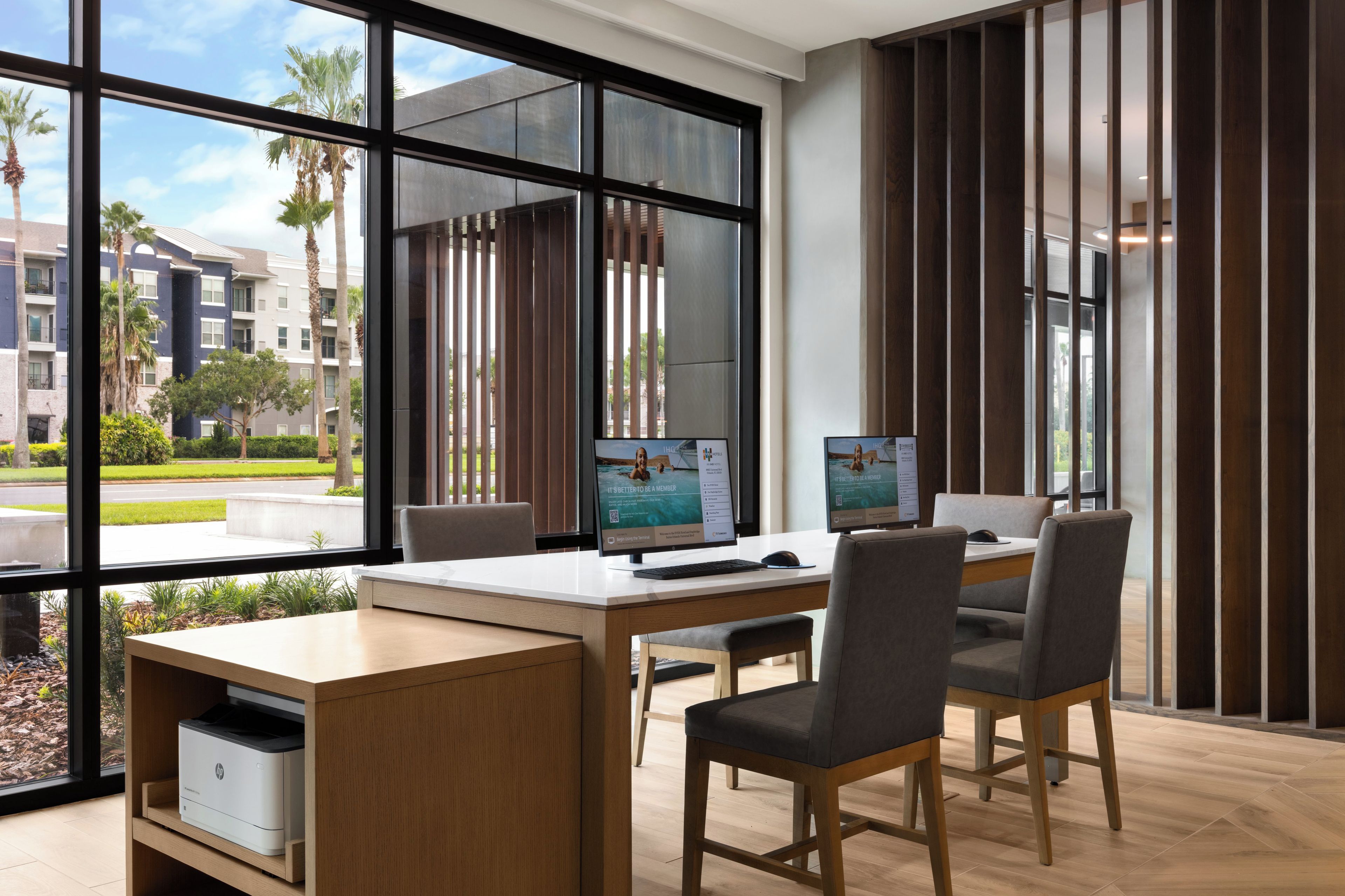 A modern office space with two desks, chairs, and large windows offering a view of a residential area.