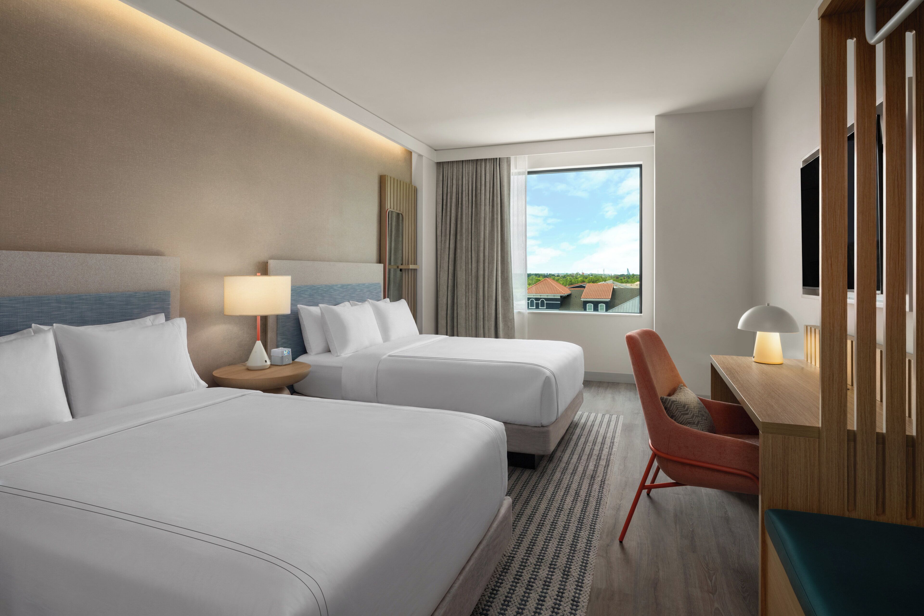 A hotel room with two beds, a desk, a chair, a window with a view, and a large mirror.