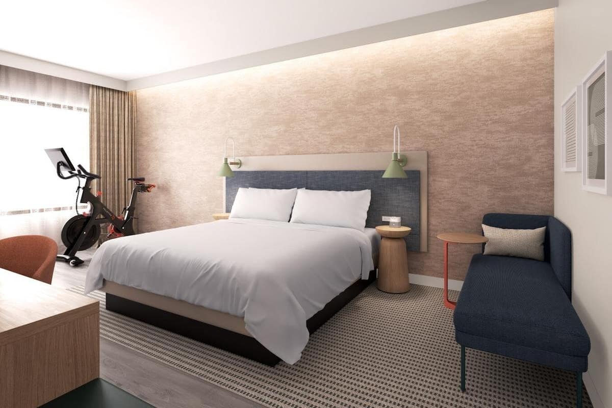 A modern hotel room with a large bed, a desk, an exercise bike, and a seating area.